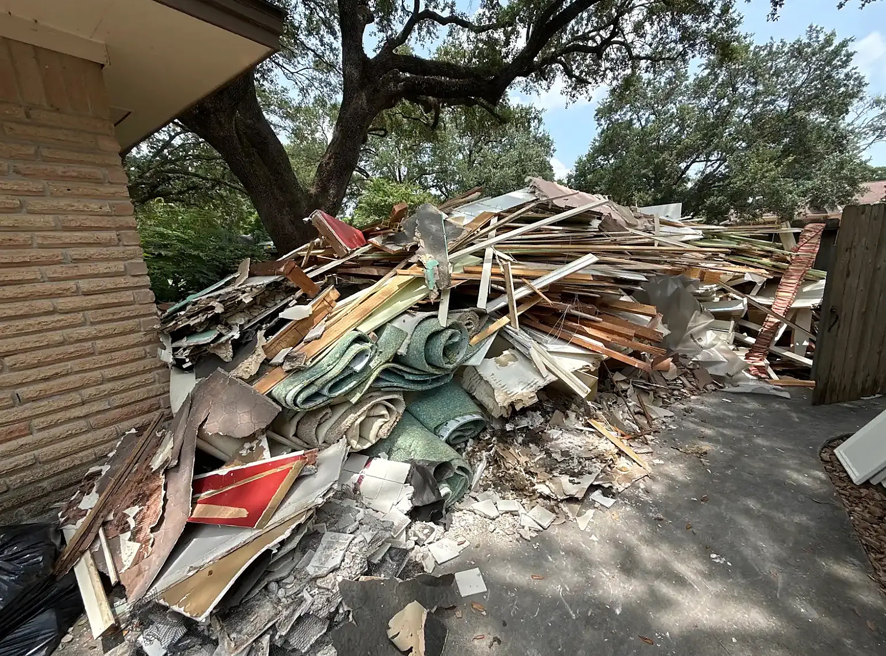Large driveway pile of lumber, carpet rolls, drywall and trim from a full home remodel tear-out